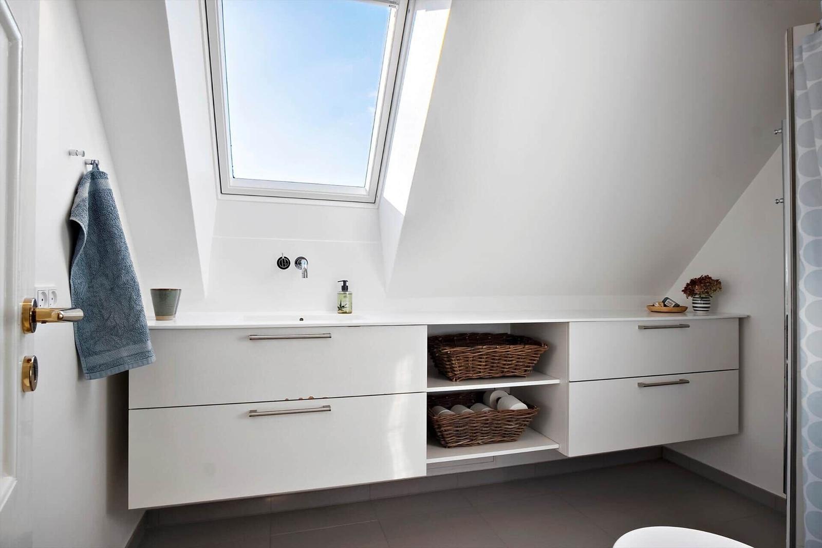 Bathroom with sloped ceiling, window, sink, and bath accessories.