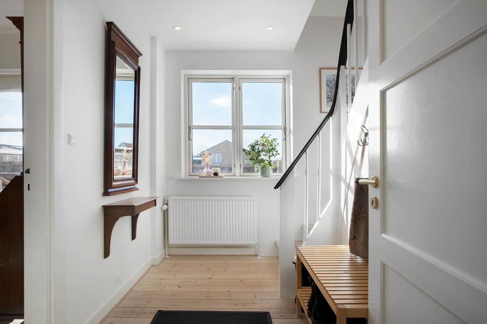 Hallway with wooden floor, mirror, and window with plant.