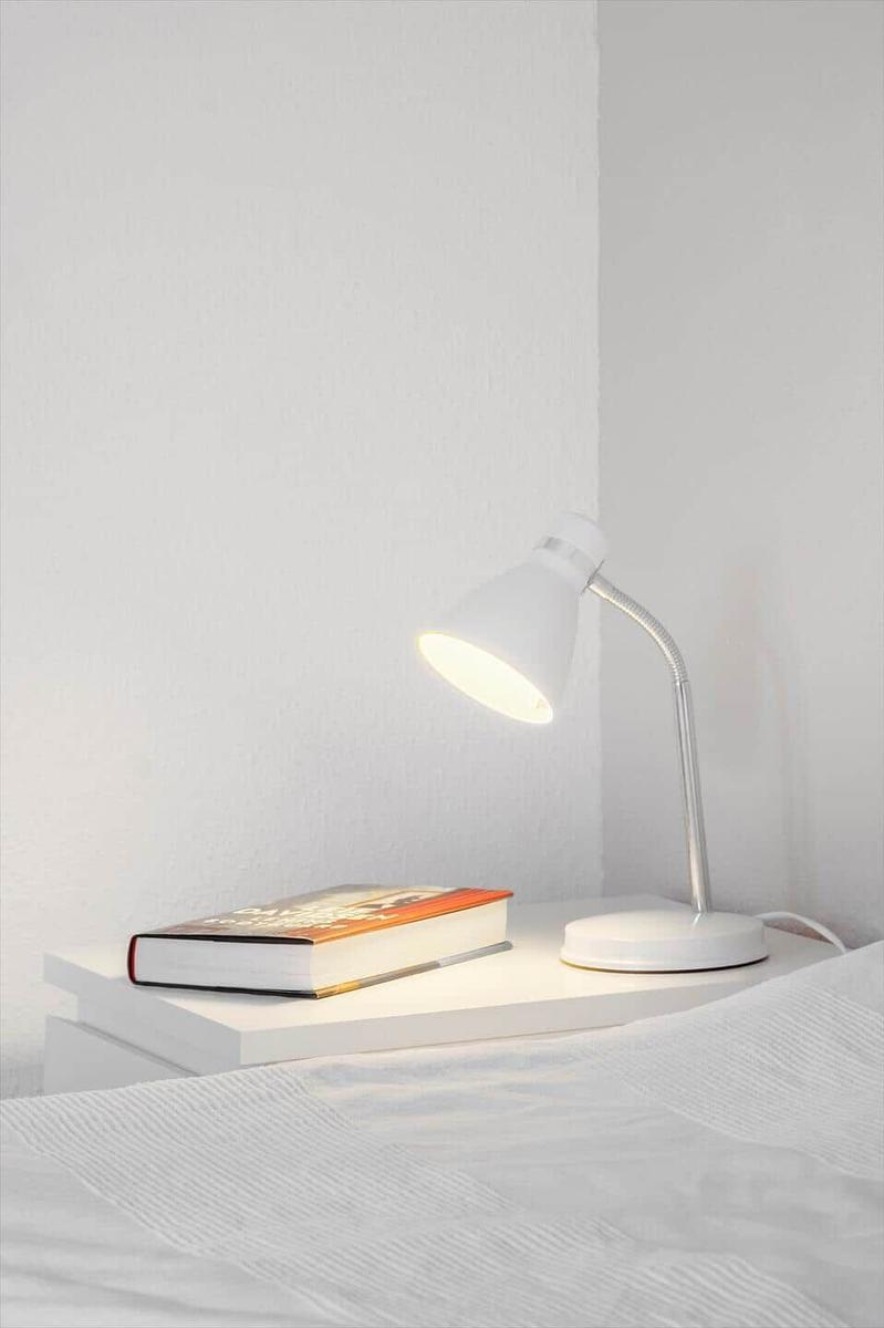 Lamp on nightstand beside bed with book.