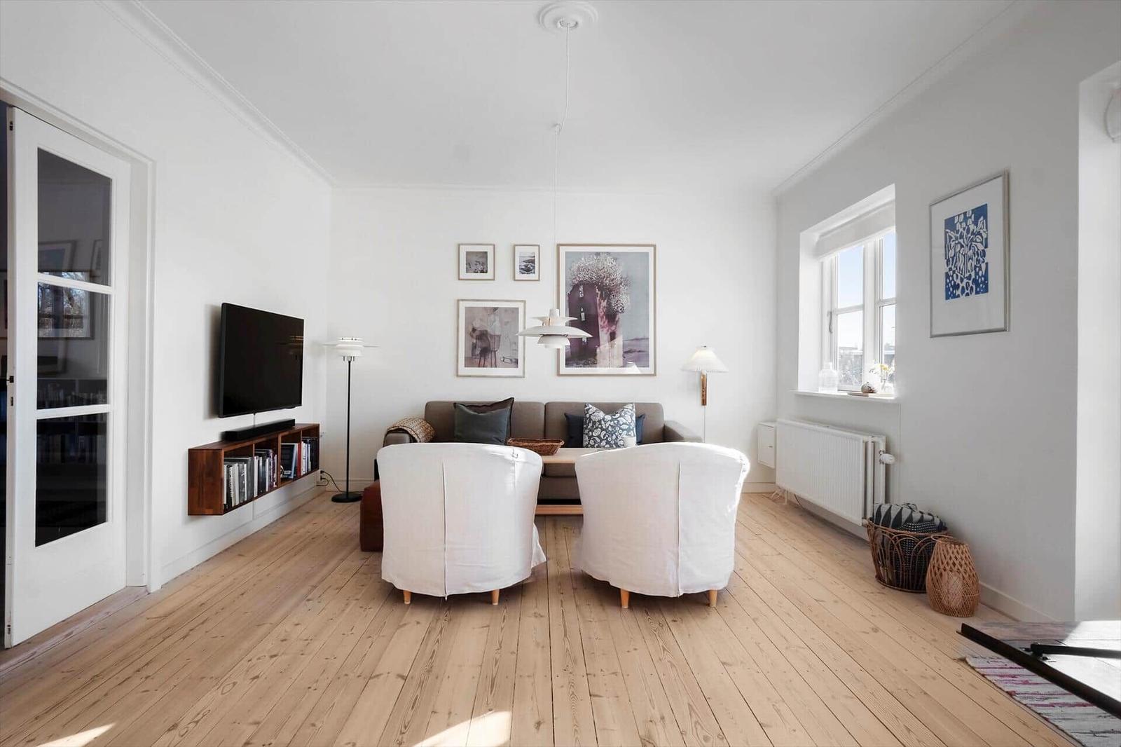 Living room with wooden floor, sofa, two white chairs, and wall art.