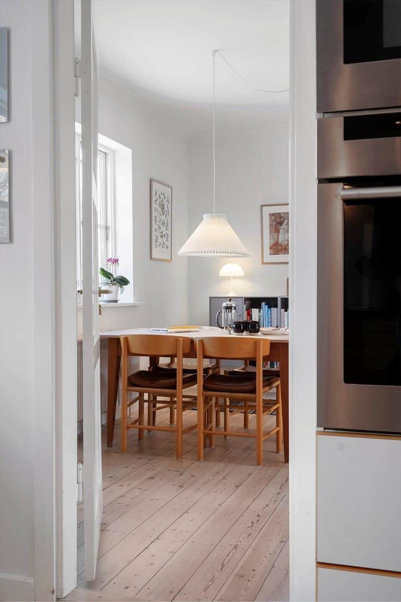 Dining area with wooden table, chairs, and window. Kitchen with stainless steel appliances.