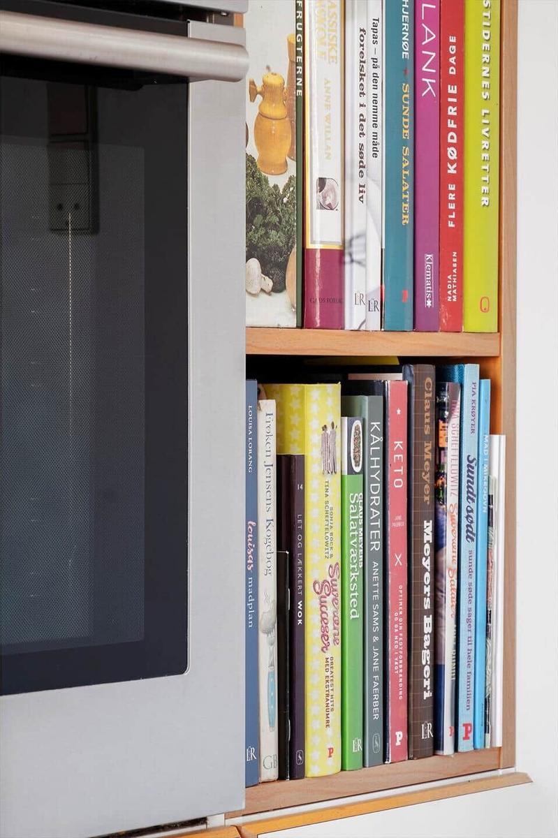 Kitchen area with built-in oven and bookshelf with cookbooks.