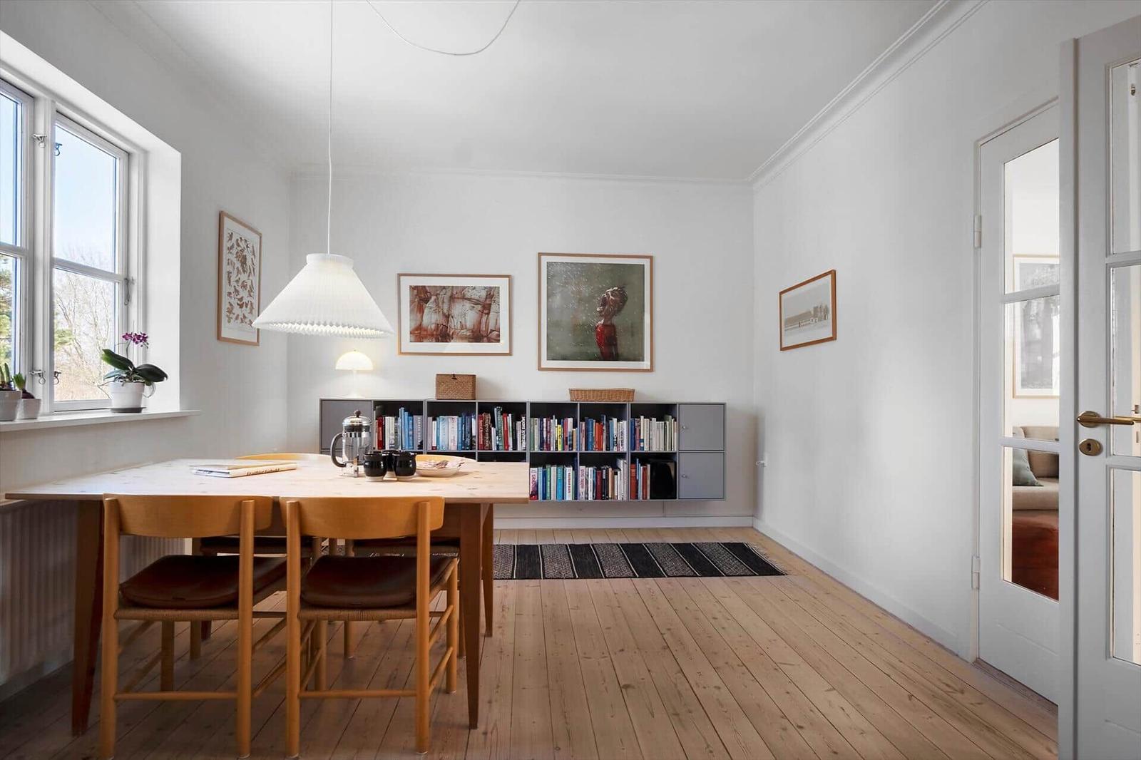 Dining room with wooden table, chairs, and bookshelf on the wall.