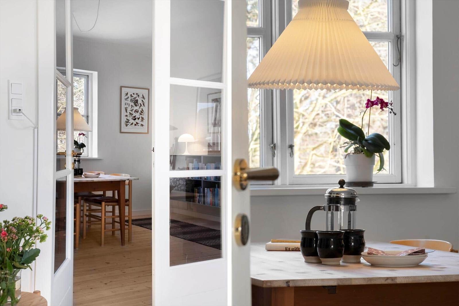 Kitchen with table, lamp, and plant. Through window and door to living room.