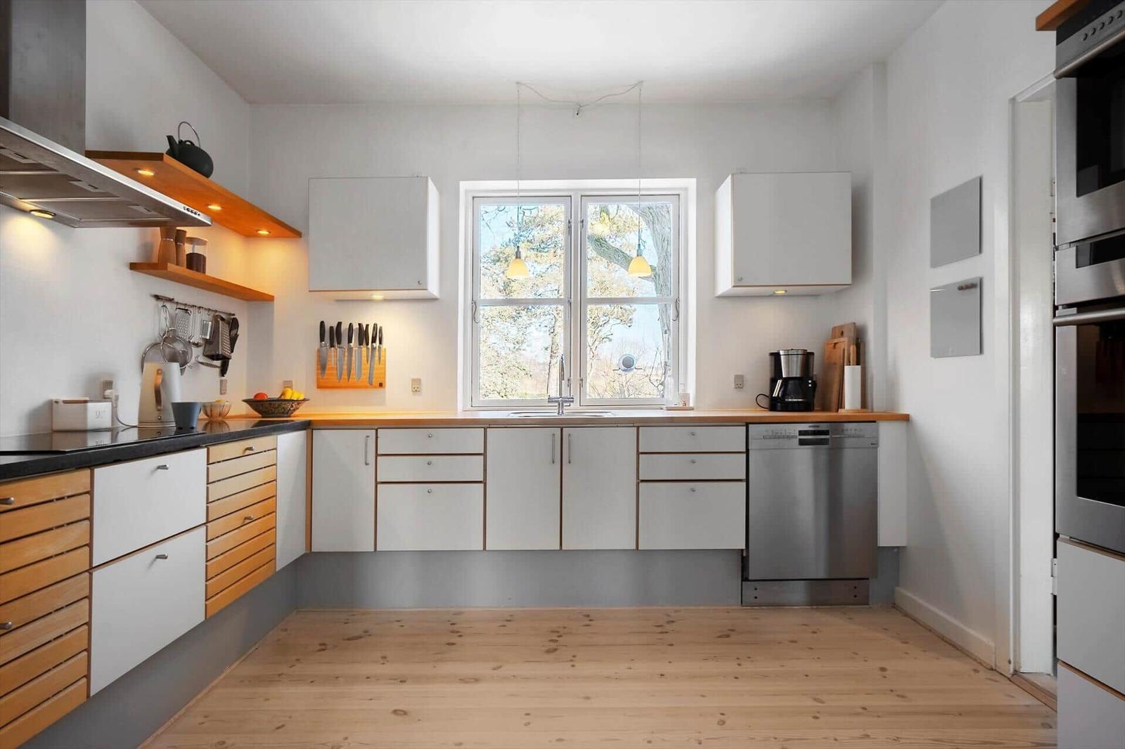 Kitchen with wooden floor, white cabinets, and window with view of trees.