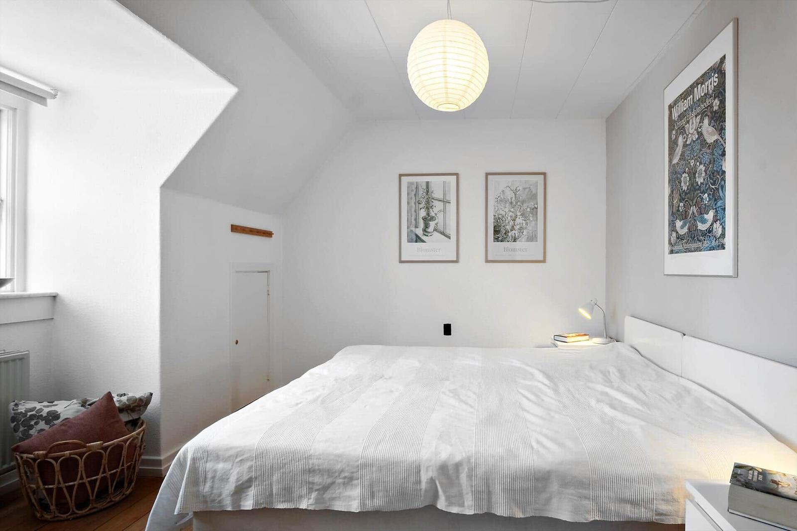 Bedroom with sloped ceiling, bed, lamp, and wall art.
