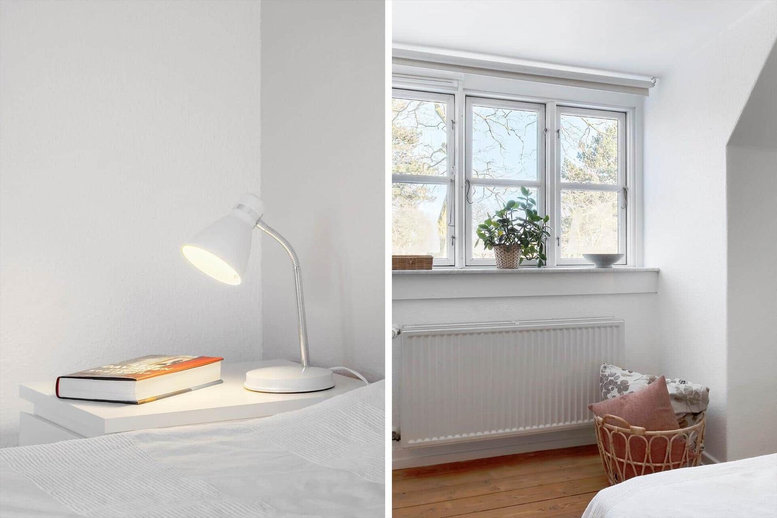 Bedroom with white nightstand, lamp, and book. Window with plant and radiator.