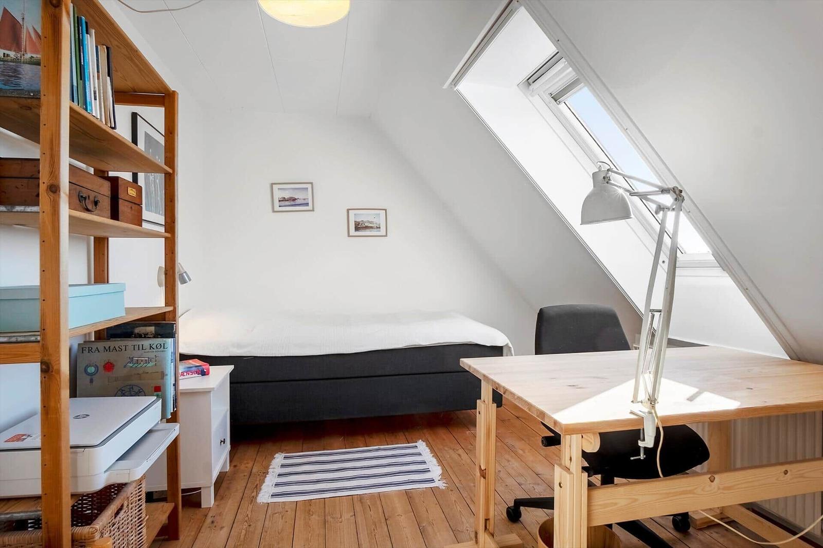 Bedroom with sloped ceiling, desk, and bookshelf.