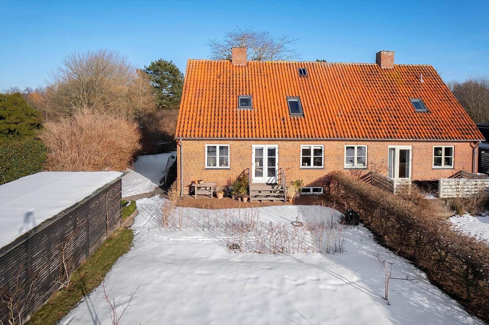 A house with red tiled roof and white entrance. The garden is covered in snow.