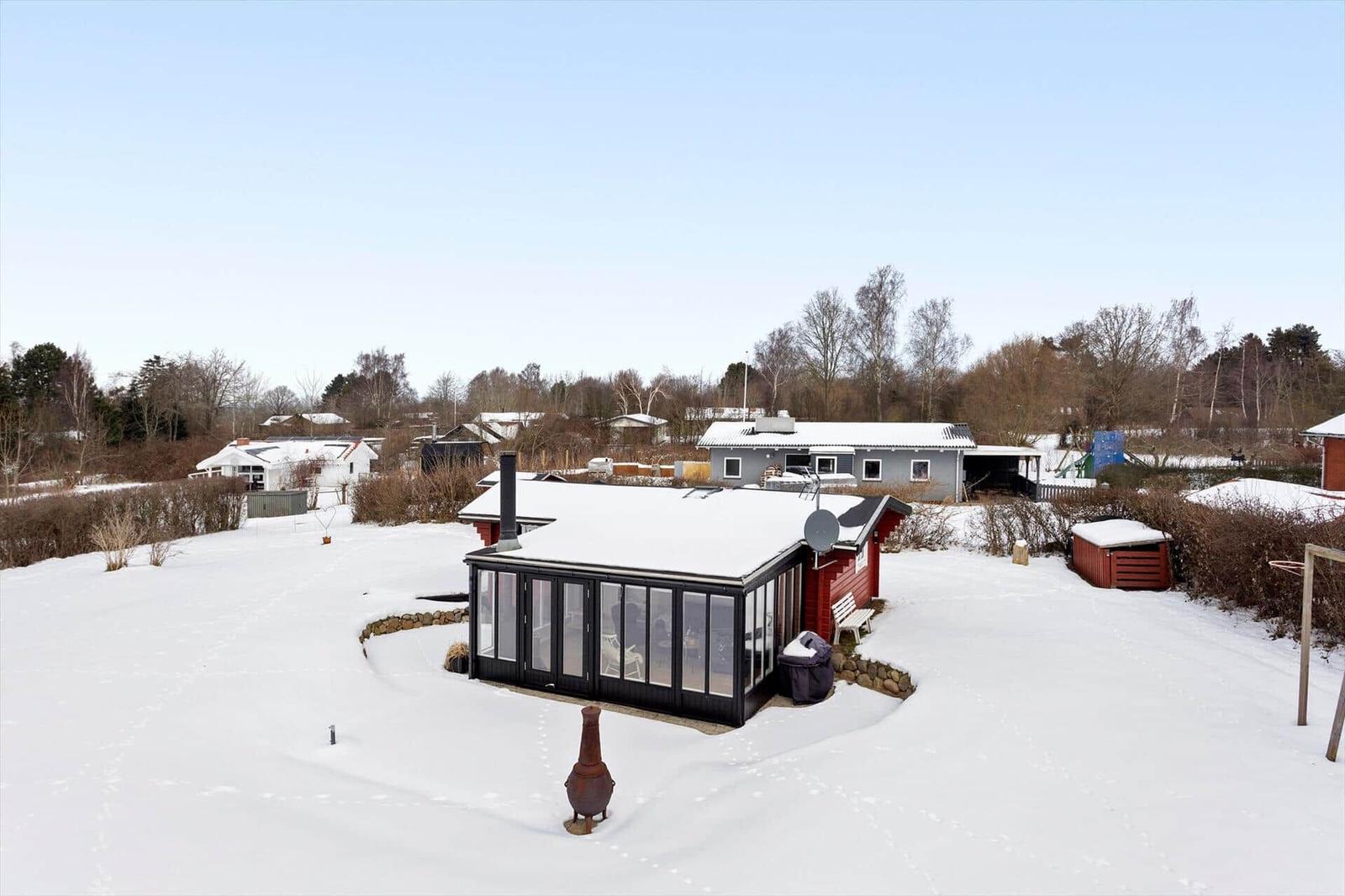 Snow-covered garden with red house and glass conservatory.