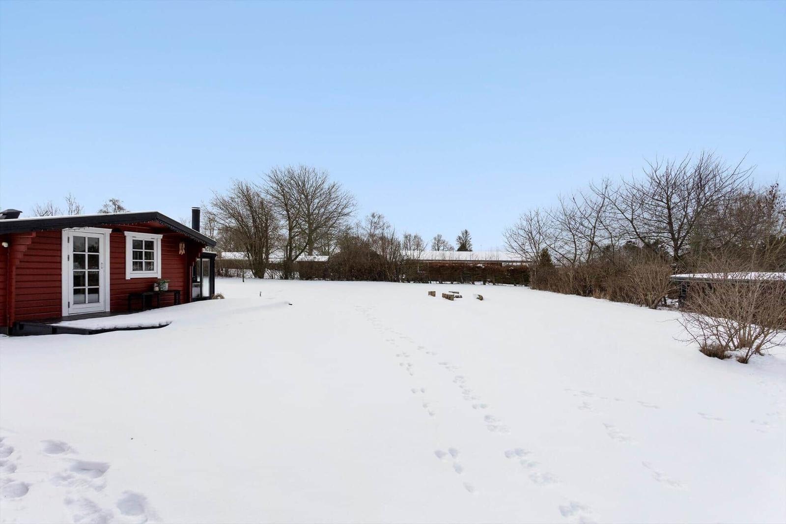 Red wooden house on snow-covered ground with footprints.