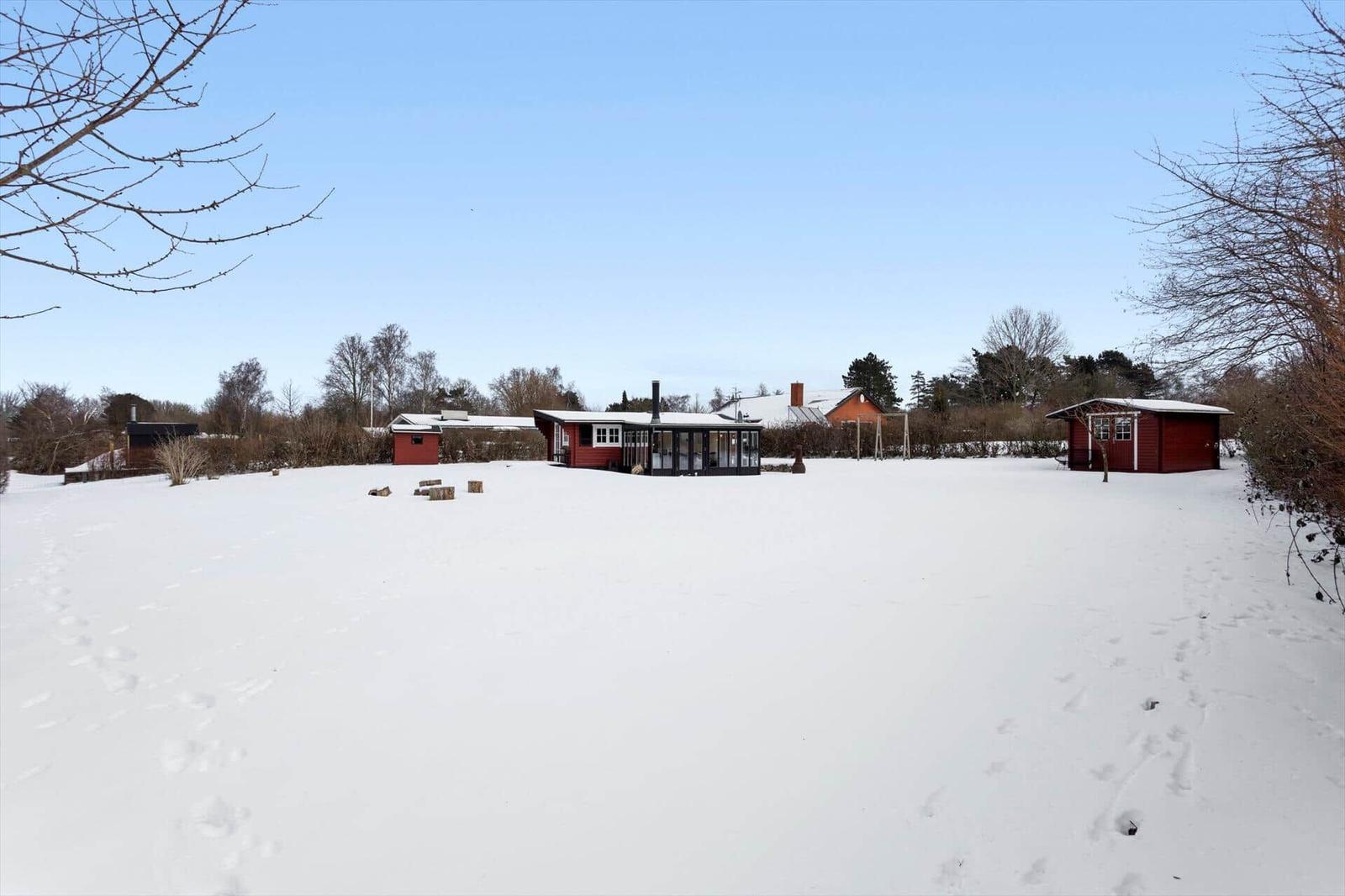 Snow-covered landscape with a red house and smaller buildings in the background.