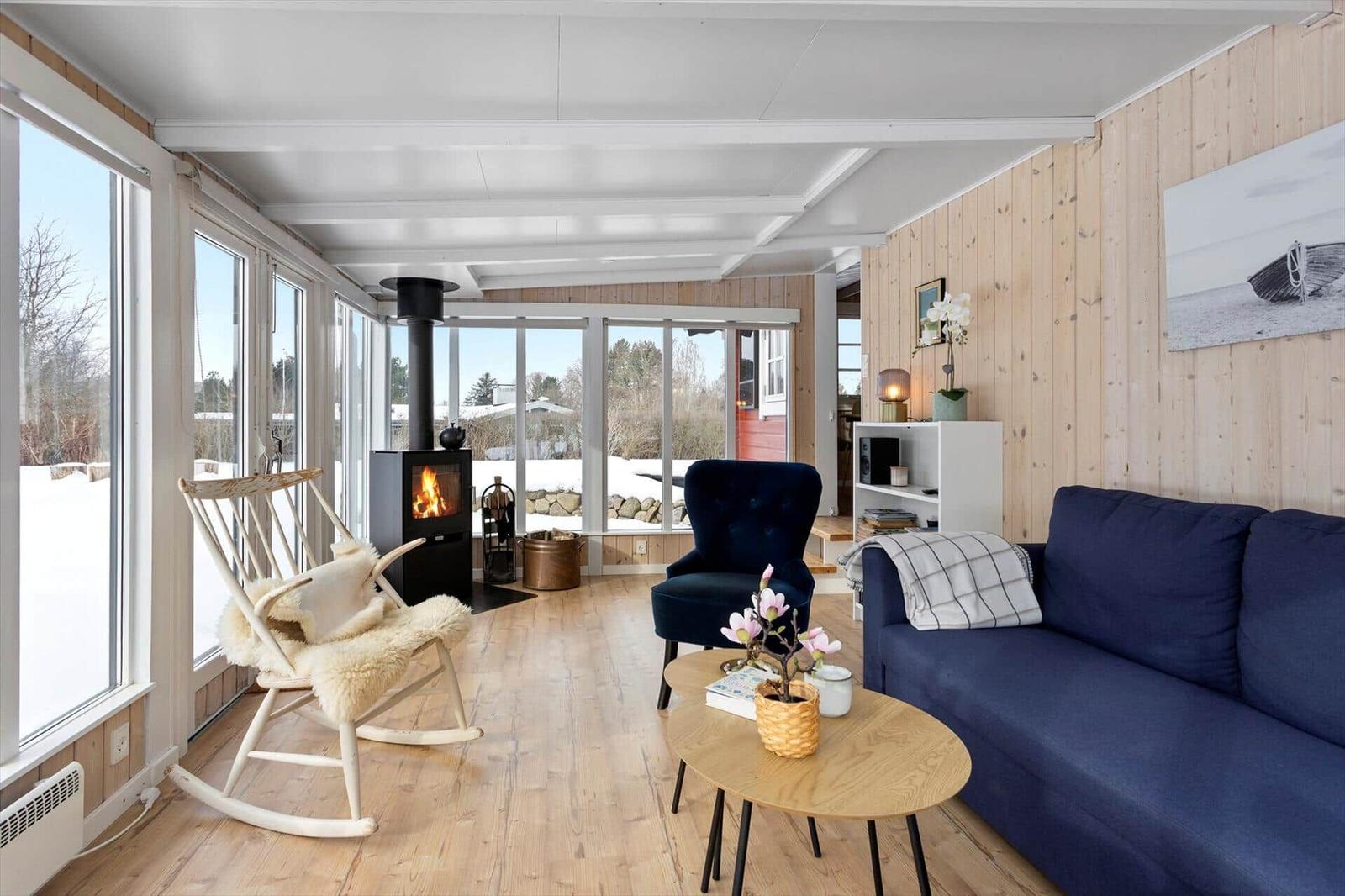 Living room with fireplace, sofa and armchair. Wooden walls and large windows.