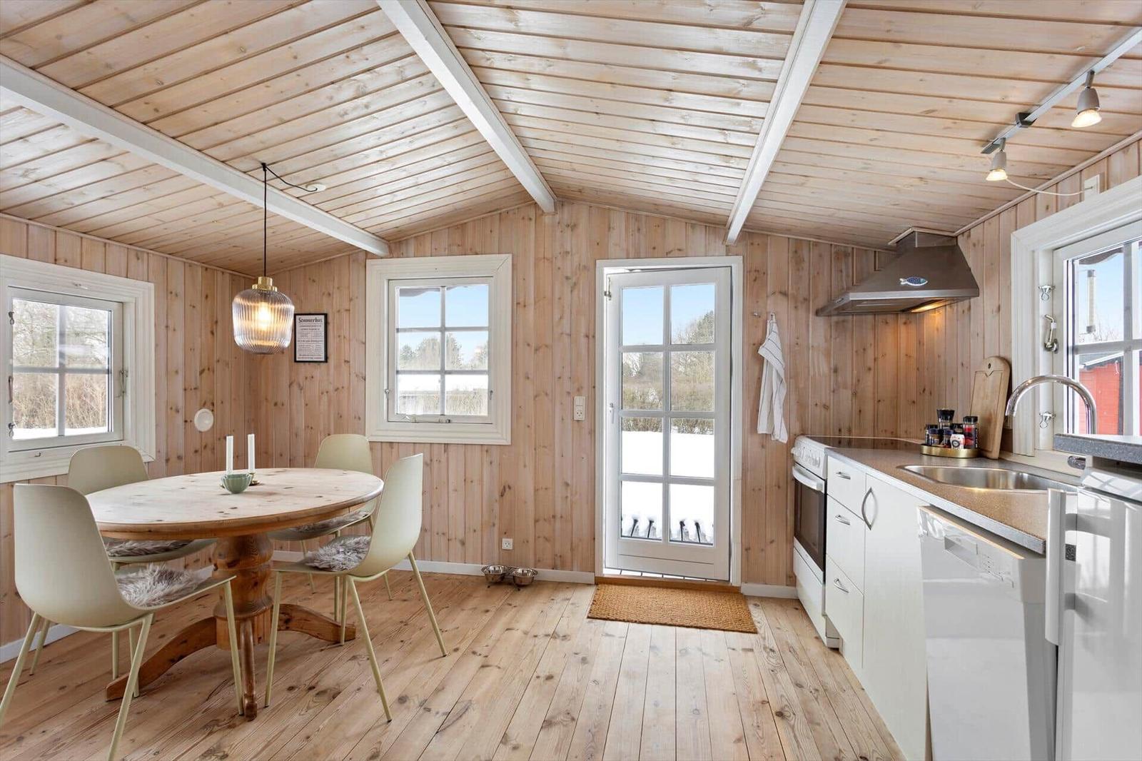 Kitchen and dining area with wooden walls, table, chairs, and windows.
