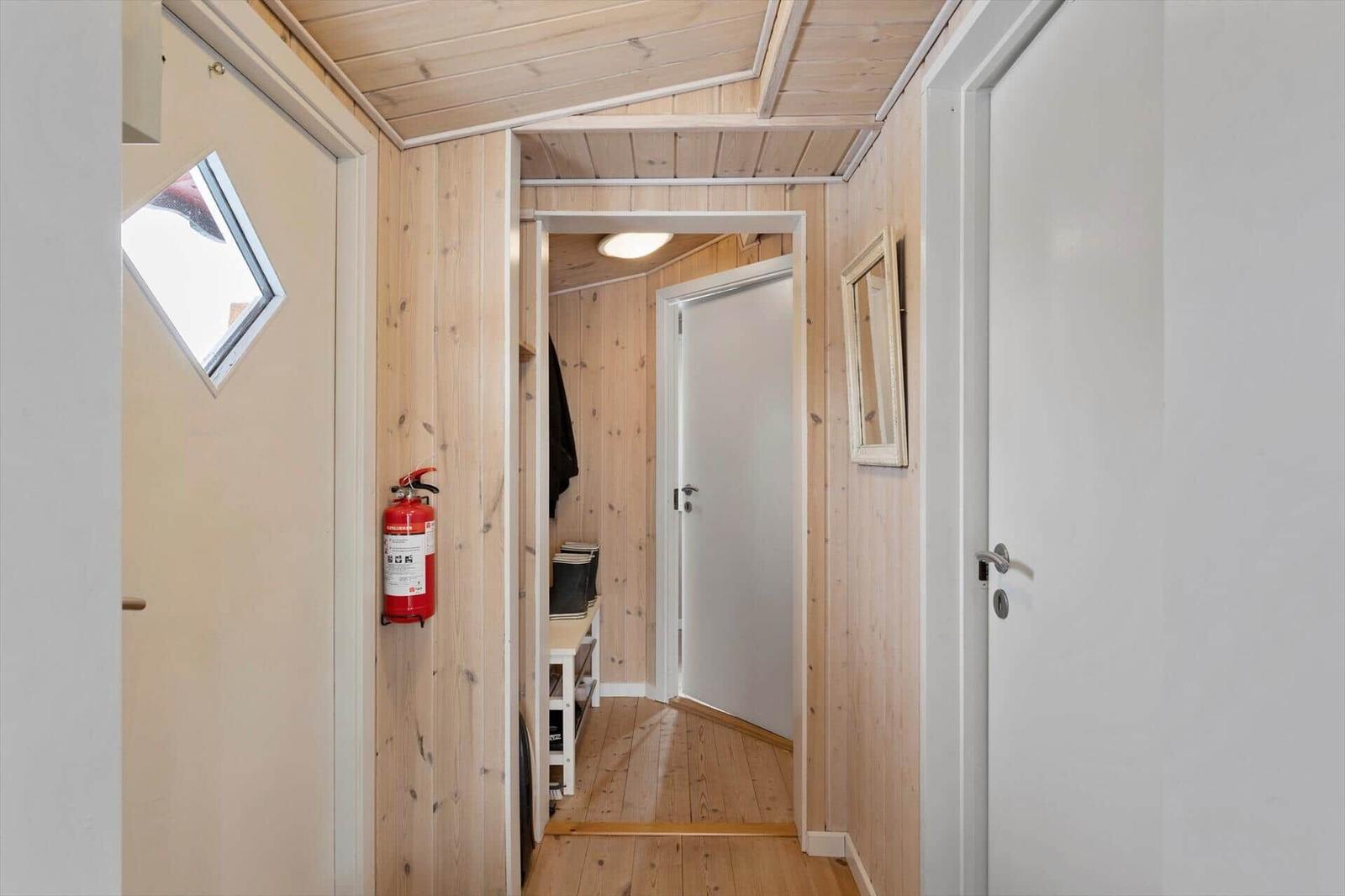 Hallway with wooden walls, fire extinguisher, and door to a room.