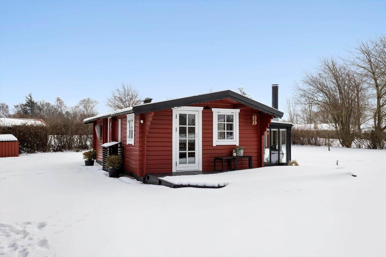 Red wooden house with white window frames covered in snow.