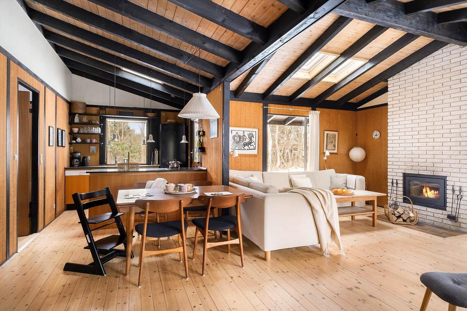Living area with fireplace, dining table, and kitchen under wooden ceiling.