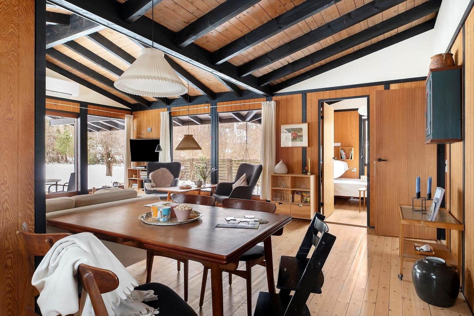 Living and dining area with wooden floor and walls. View into bedroom.