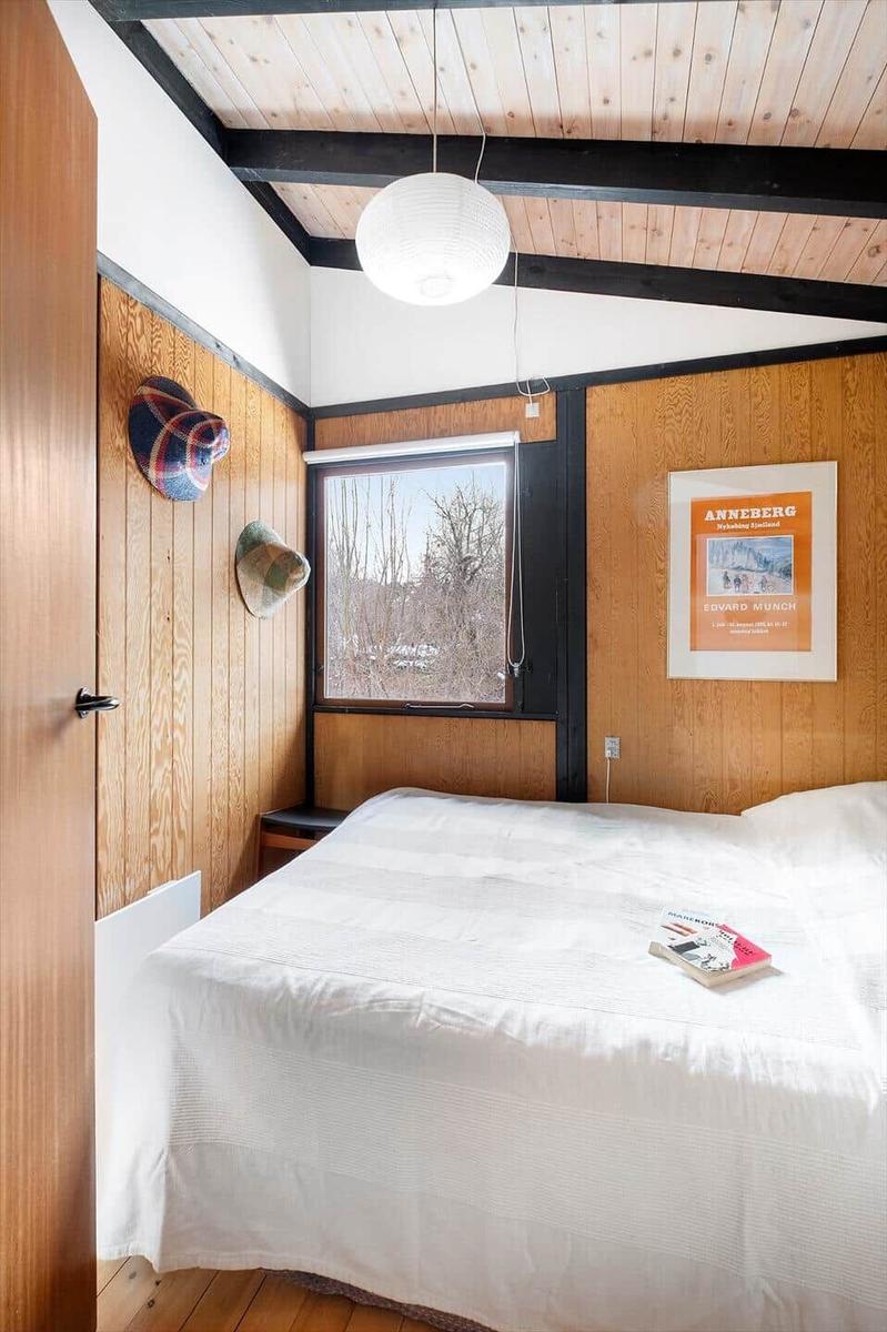 Bedroom with wooden walls, window, and bed with white bedding.