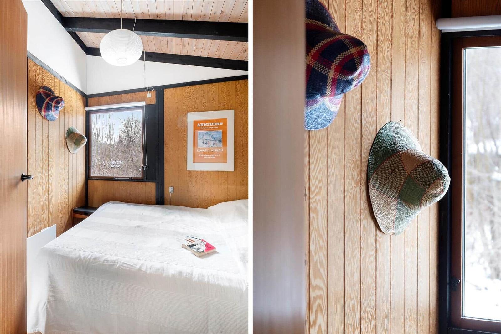 Bedroom with wooden walls, bed, and window. Hats hang on the wall.