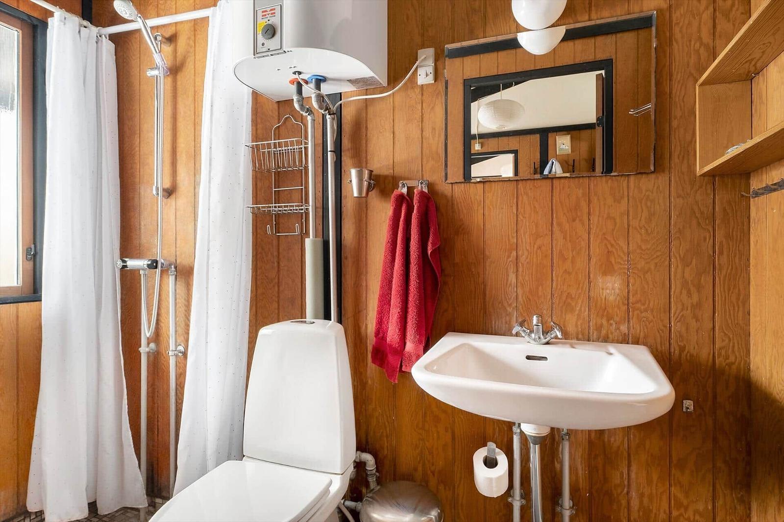 Bathroom with shower, sink, and toilet against wooden wall.