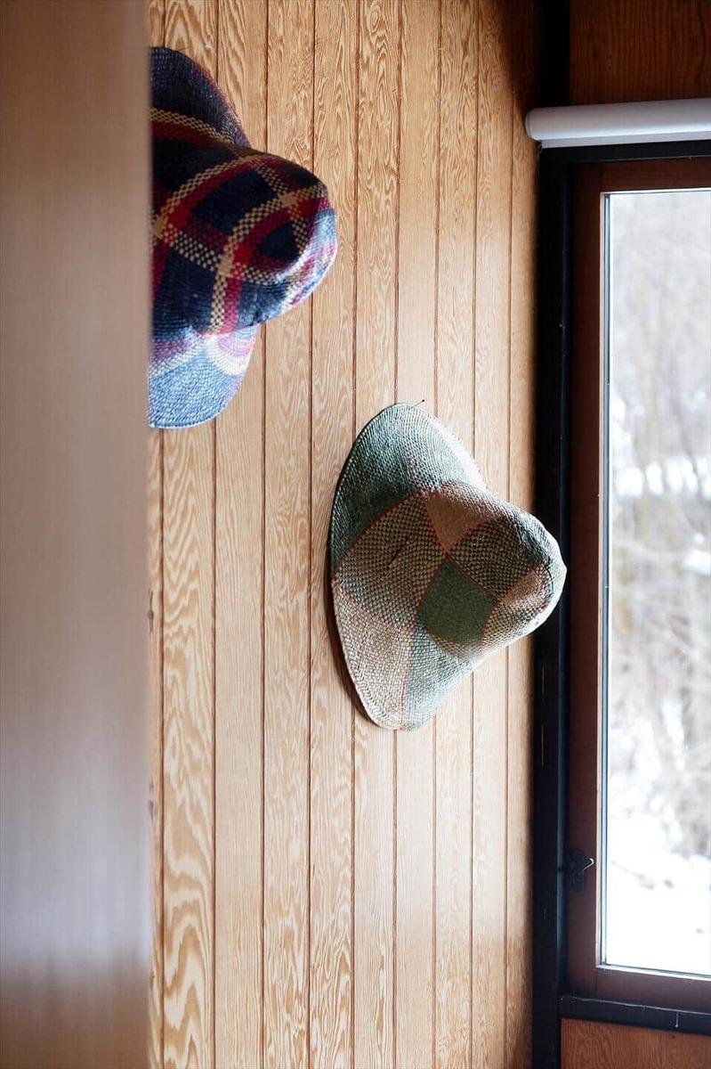 Two hats hang on a wooden wall next to a window with a view of snow.