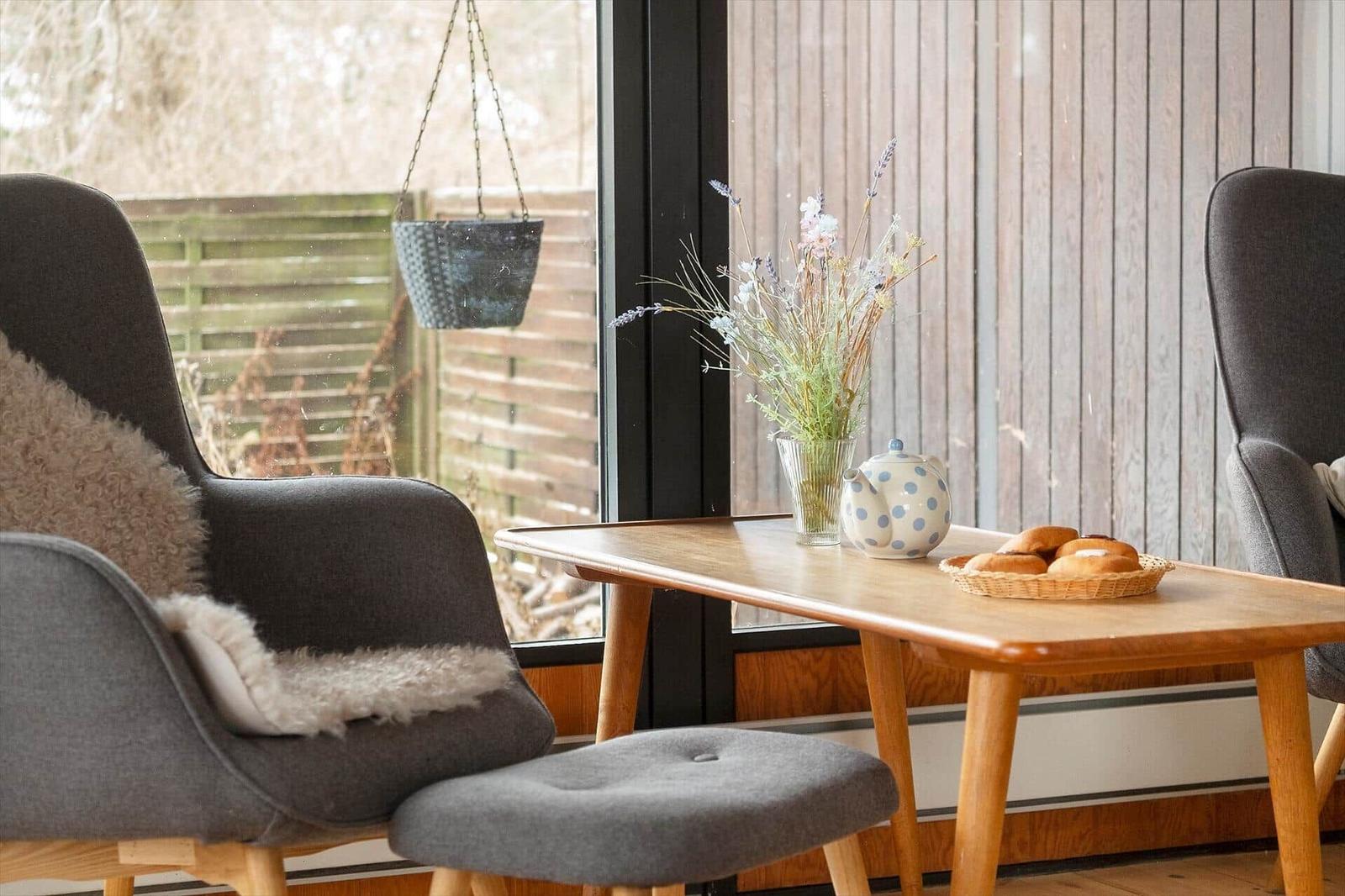 Table with teapot, bread, and flowers by window overlooking garden.
