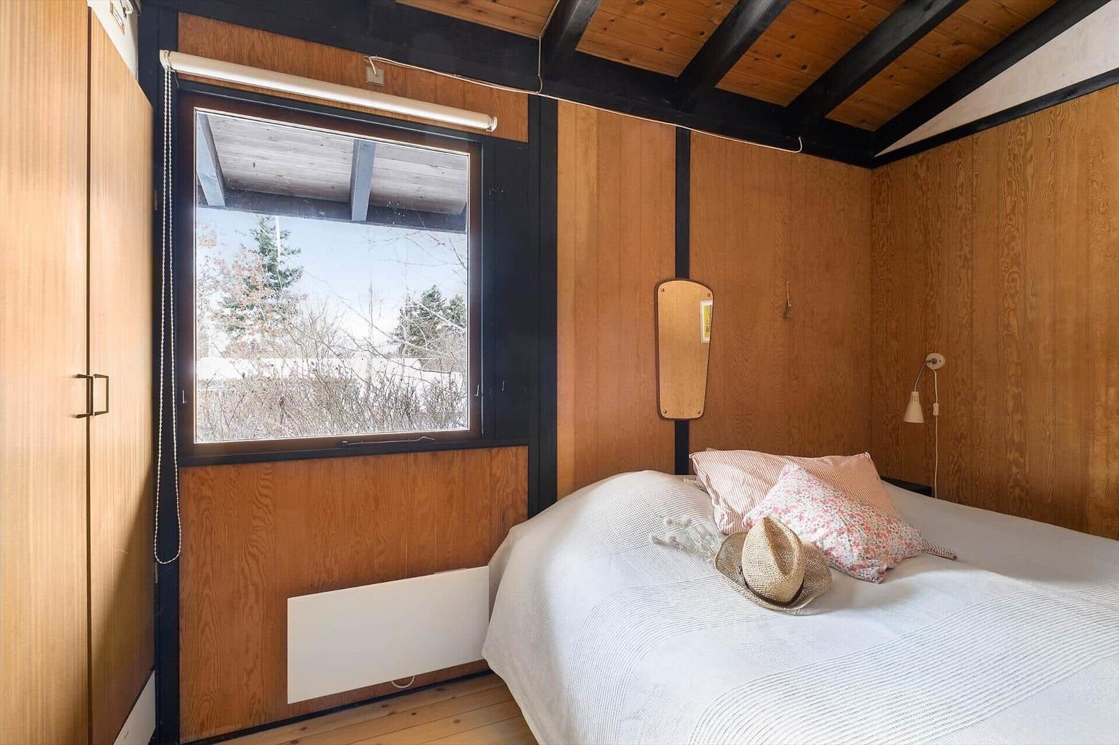 Bedroom with wooden walls, window, and bed with pillows.