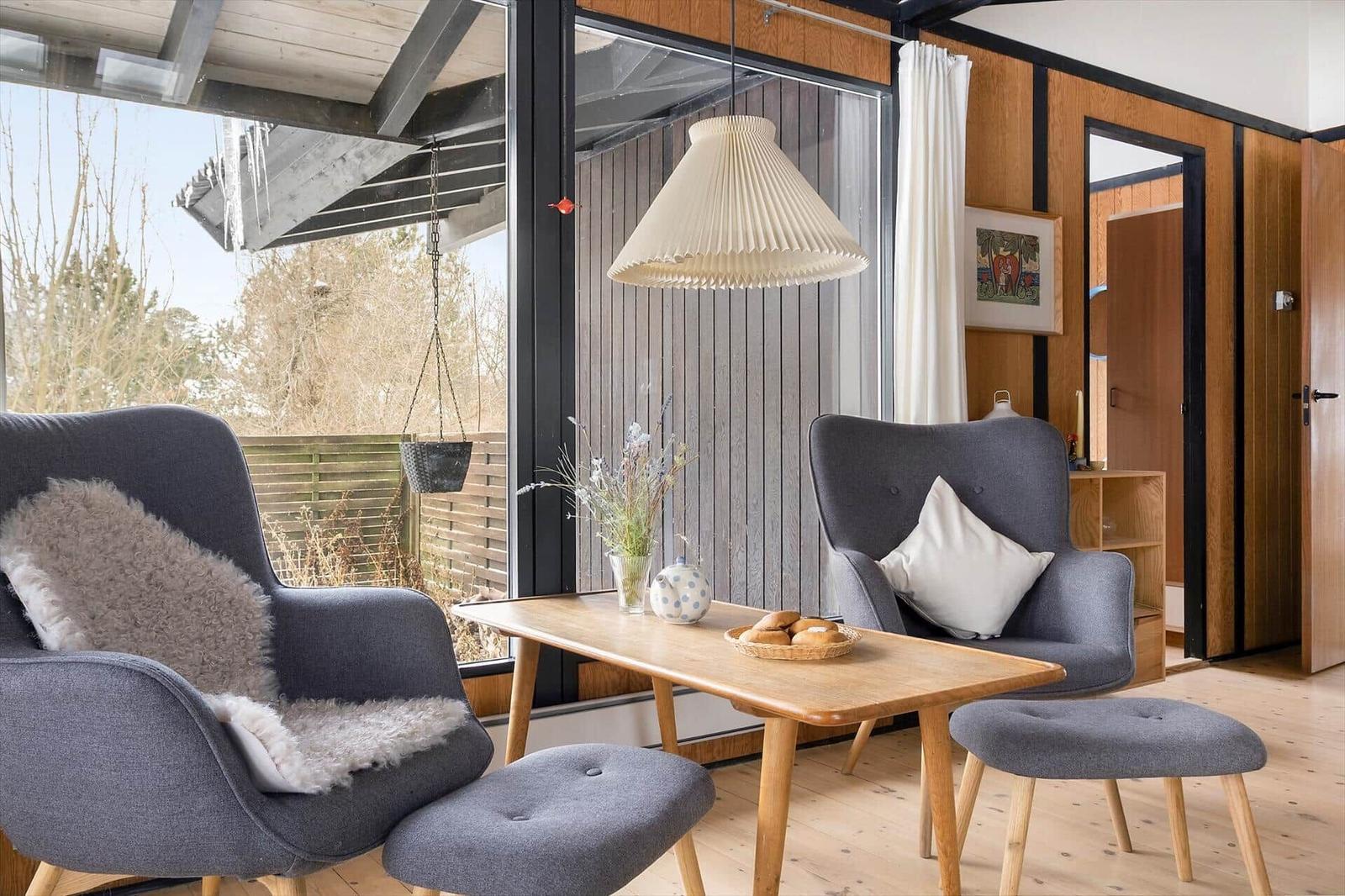 Two gray armchairs with cushions and stools around a wooden table with breakfast.
