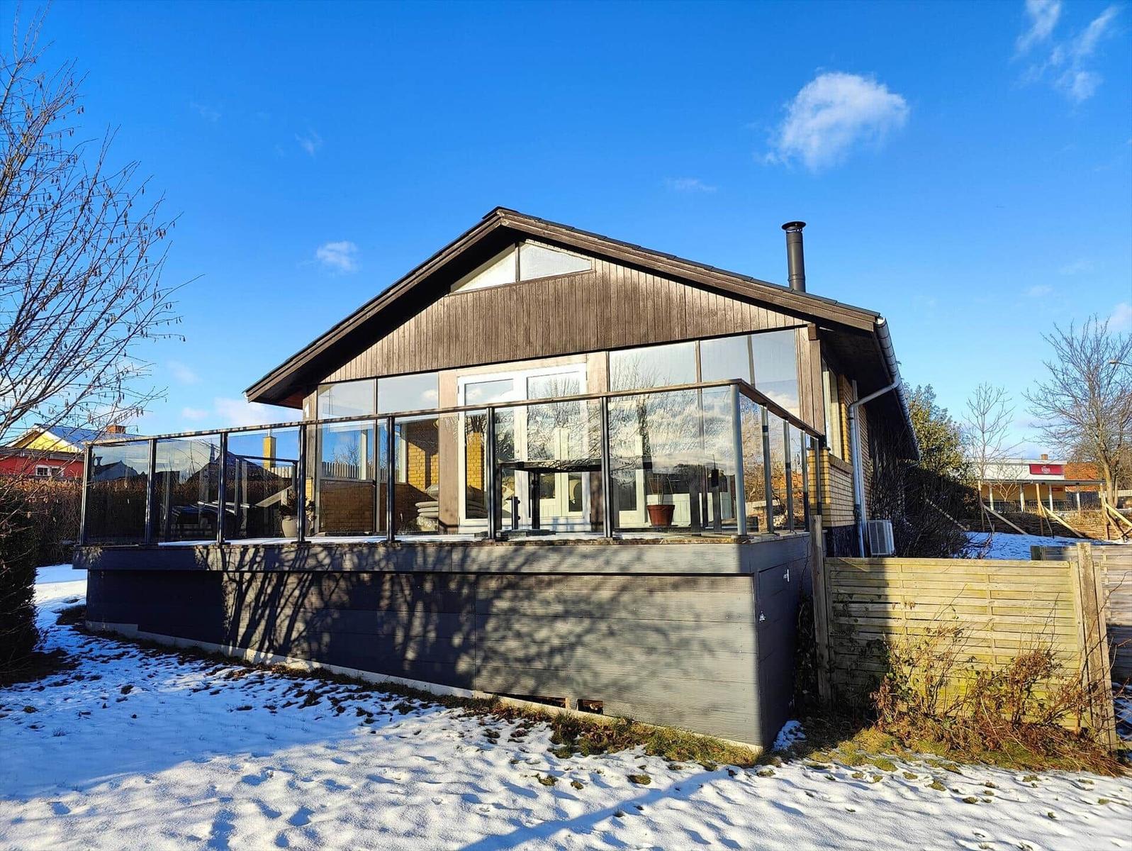 Modern wooden cabin with glass railing and snow in the front yard.