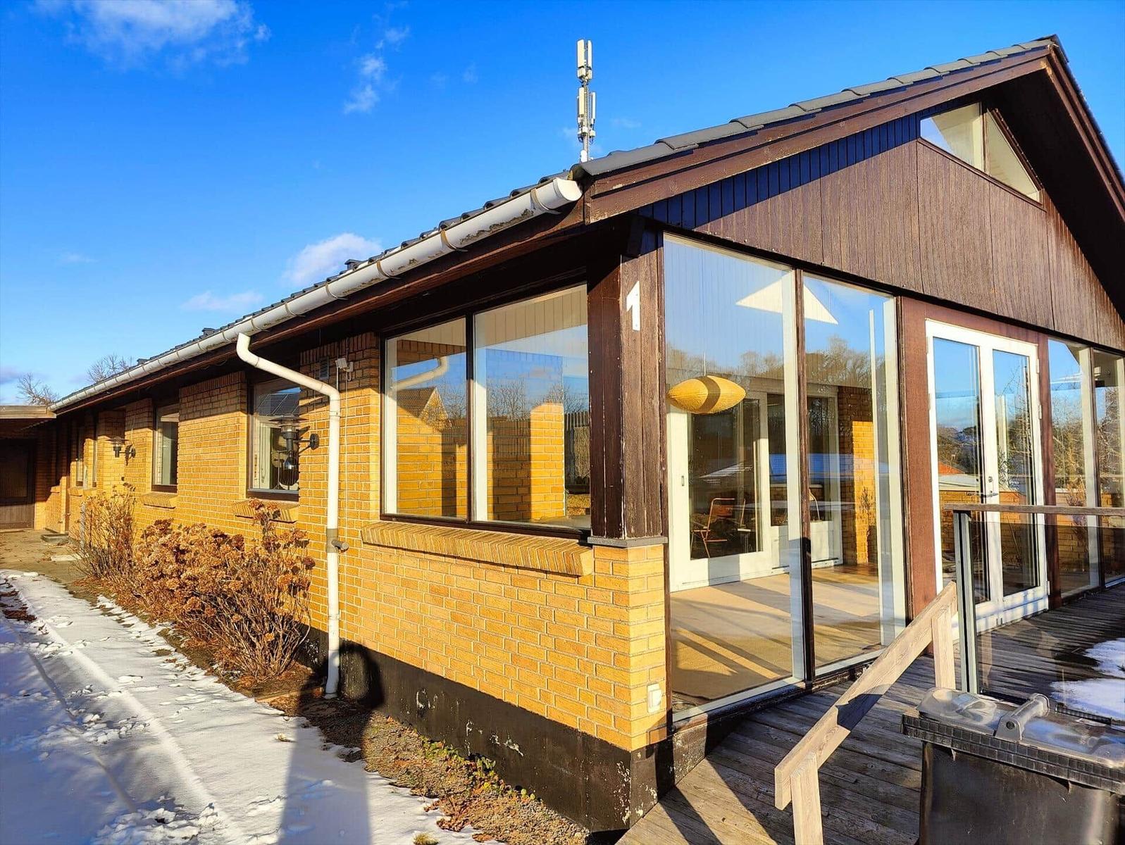 Modern vacation home with wooden facade and large glass windows. Wooden terrace with railing. Snow on ground.