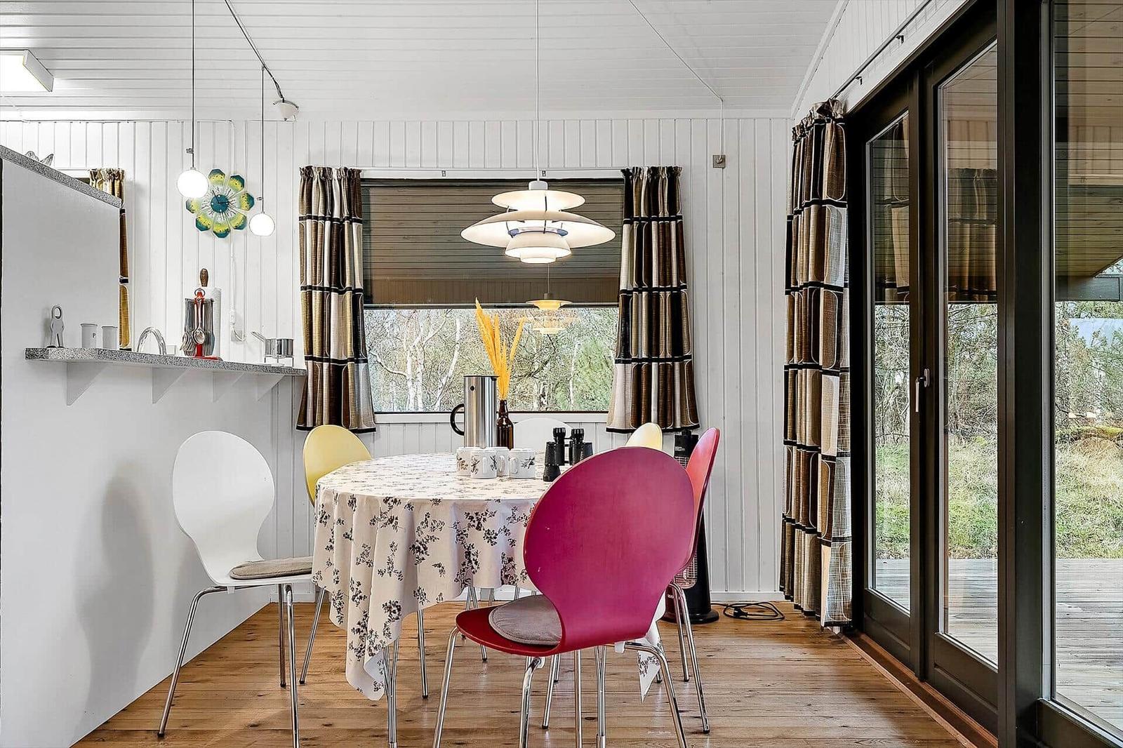 Essbereich mit runden Tisch und bunten Stühlen. Fenster und Glastür mit Vorhängen.
