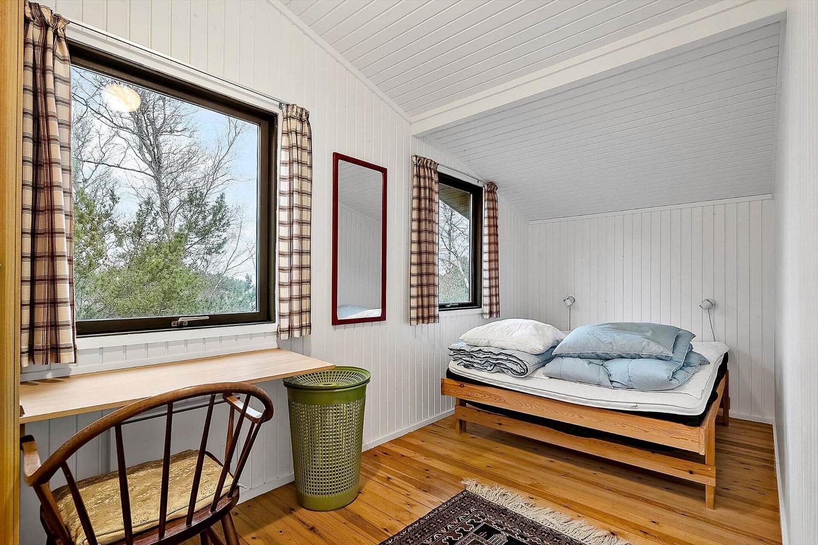 Schlafzimmer mit Bett, Schreibtisch und Fenster mit Blick auf Wald.