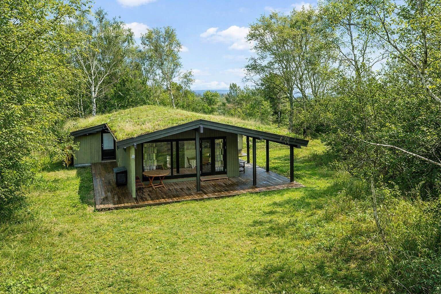 Moderne Hütte mit grünem Dach und Holzterrasse inmitten von Bäumen.