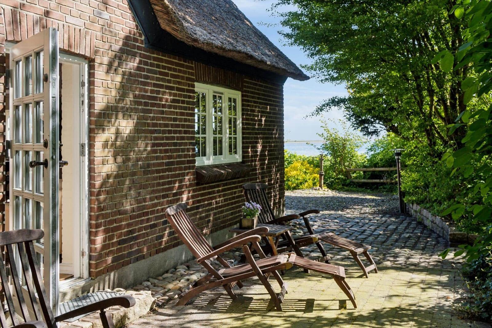 Haus mit Dach aus Stroh, Terrasse mit Liegestühlen und Blick auf Wasser.
