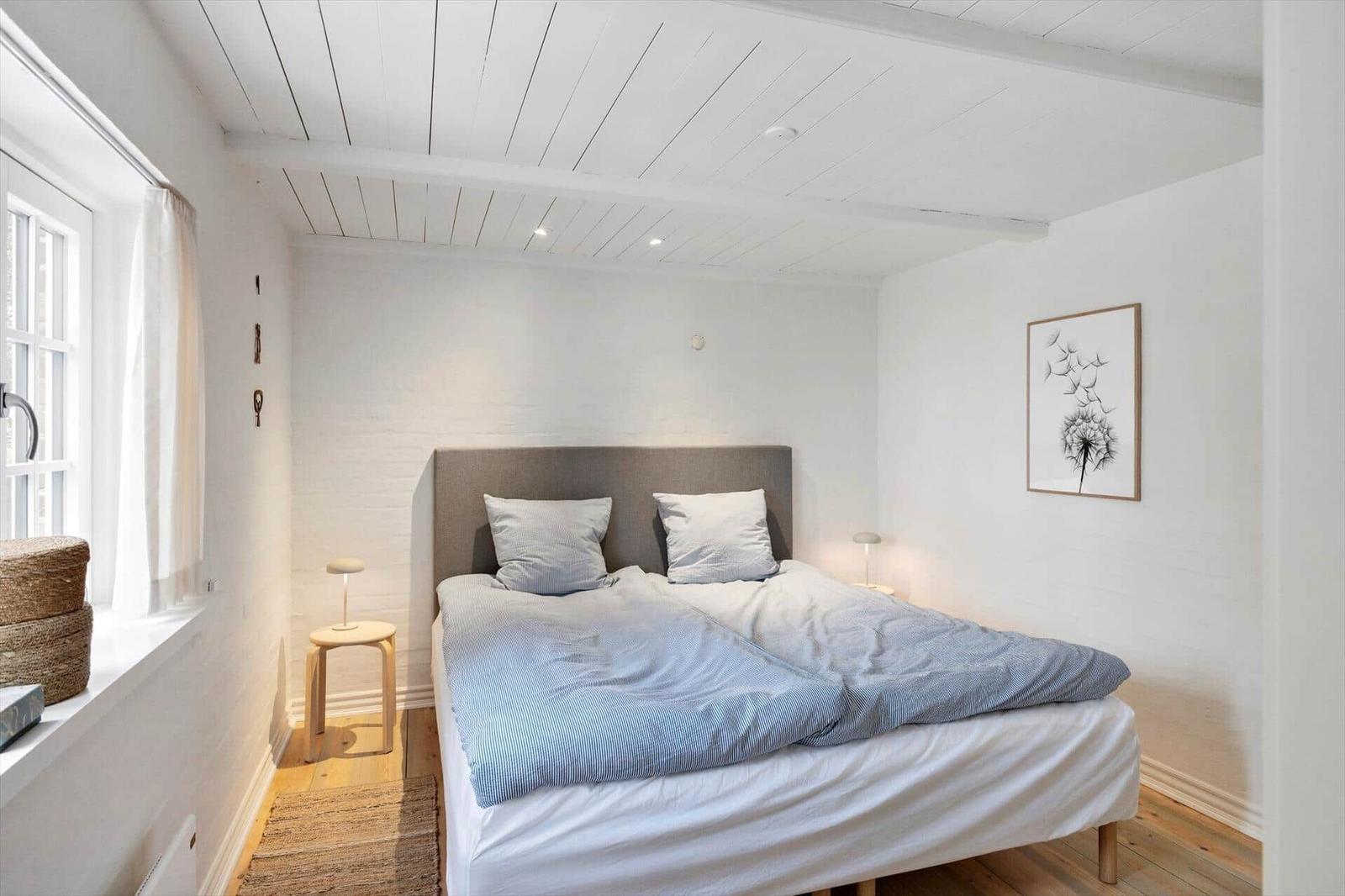 Schlafzimmer mit Bett, Fenster und Wandbild.