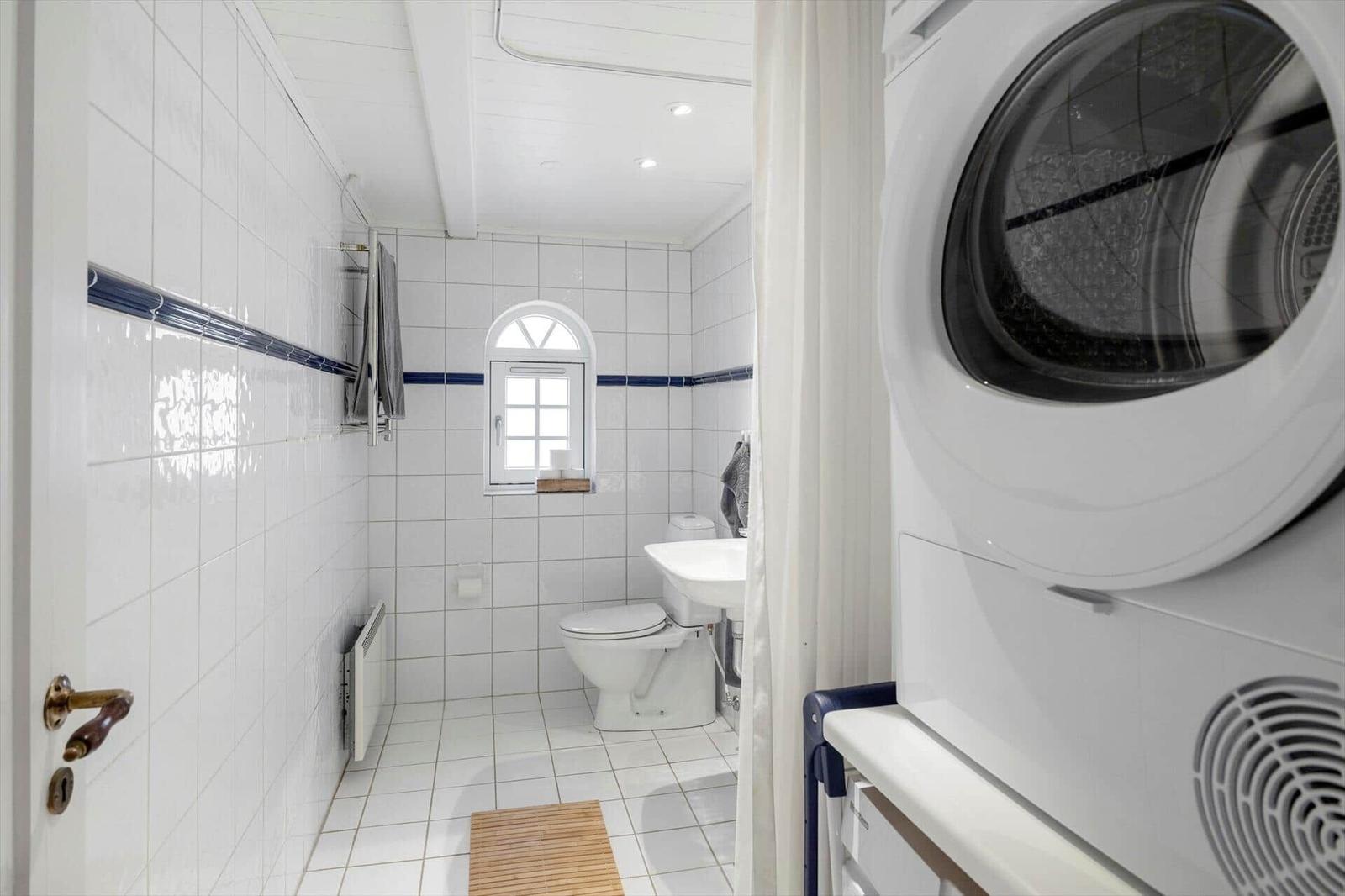 Badezimmer mit Toilette, Waschbecken und Fenster. Weiße Fliesen und Waschmaschine.