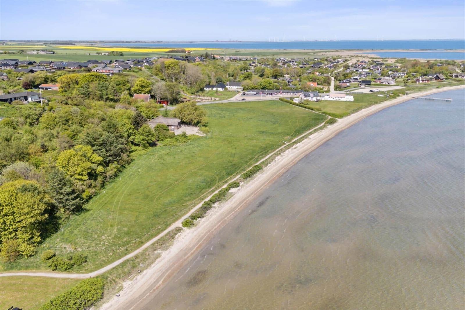 Aeriale Aufnahme einer Küstenlandschaft mit Grünflächen, Häusern und einem Strand.