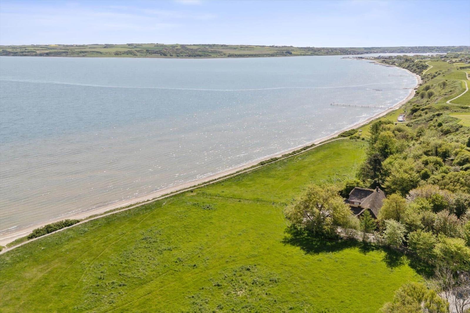 Haus am Ufer mit Blick auf das Wasser und grüne Wiesen.