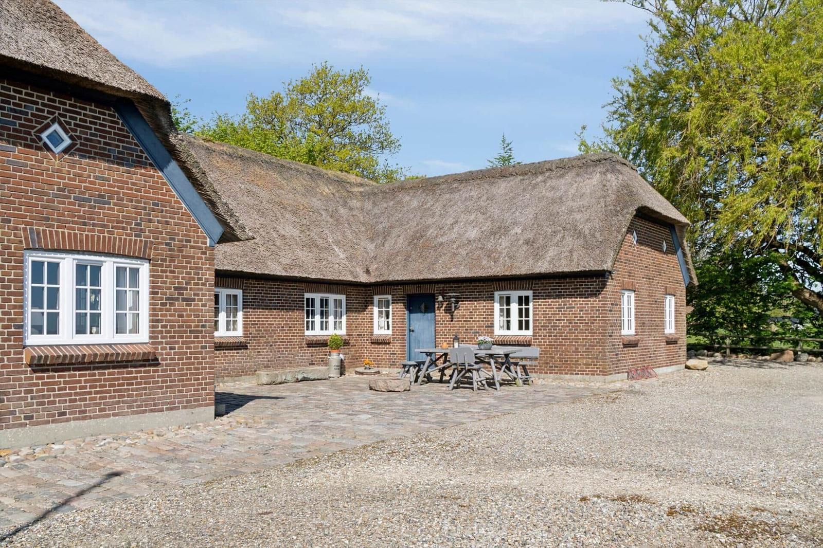 Haus mit Strohdach, Steinplattenhof und Holztisch mit Bänken.