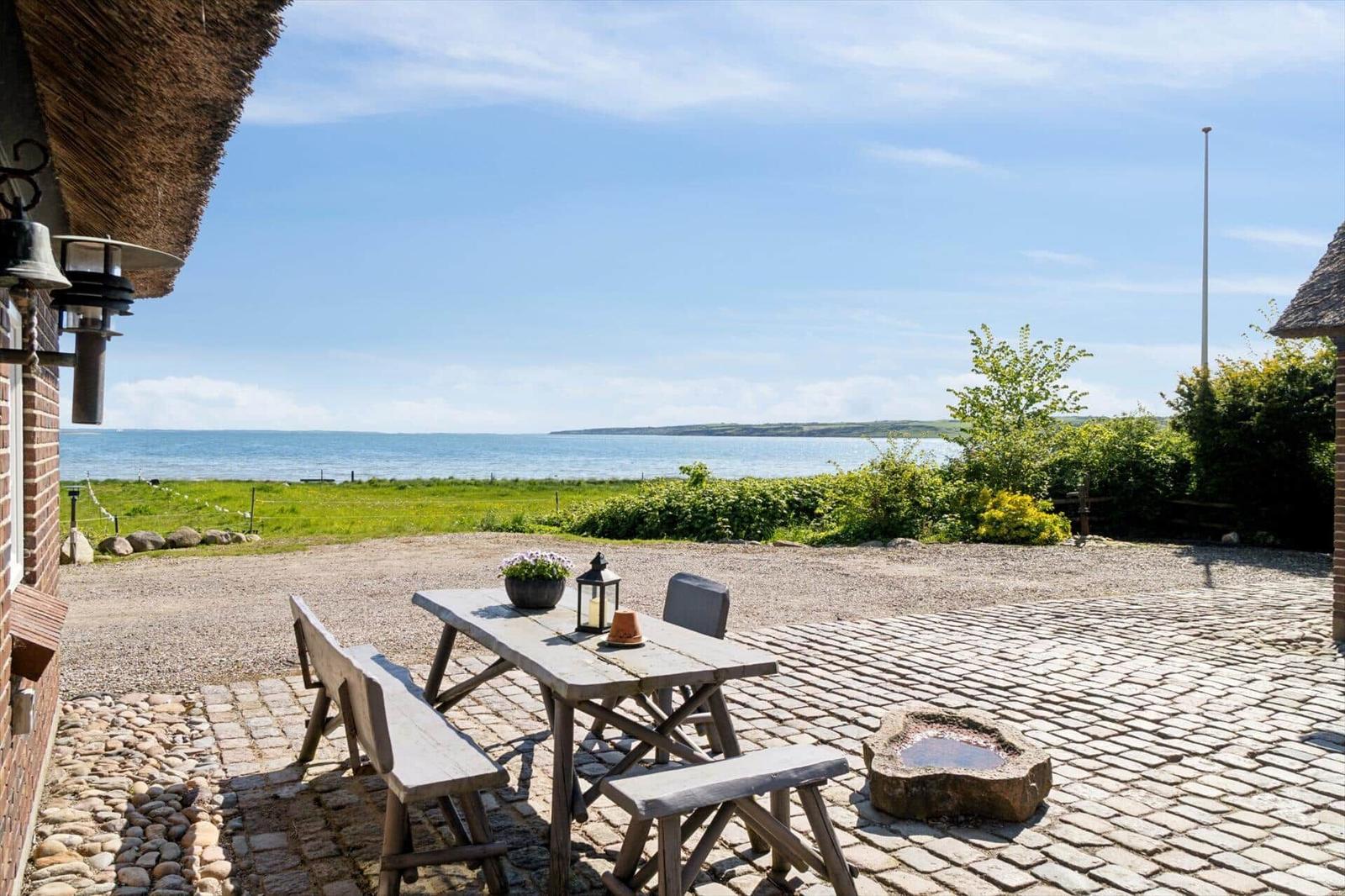 Holztisch mit Bänken auf Kiesfläche, Blick auf Meer und Grünfläche.