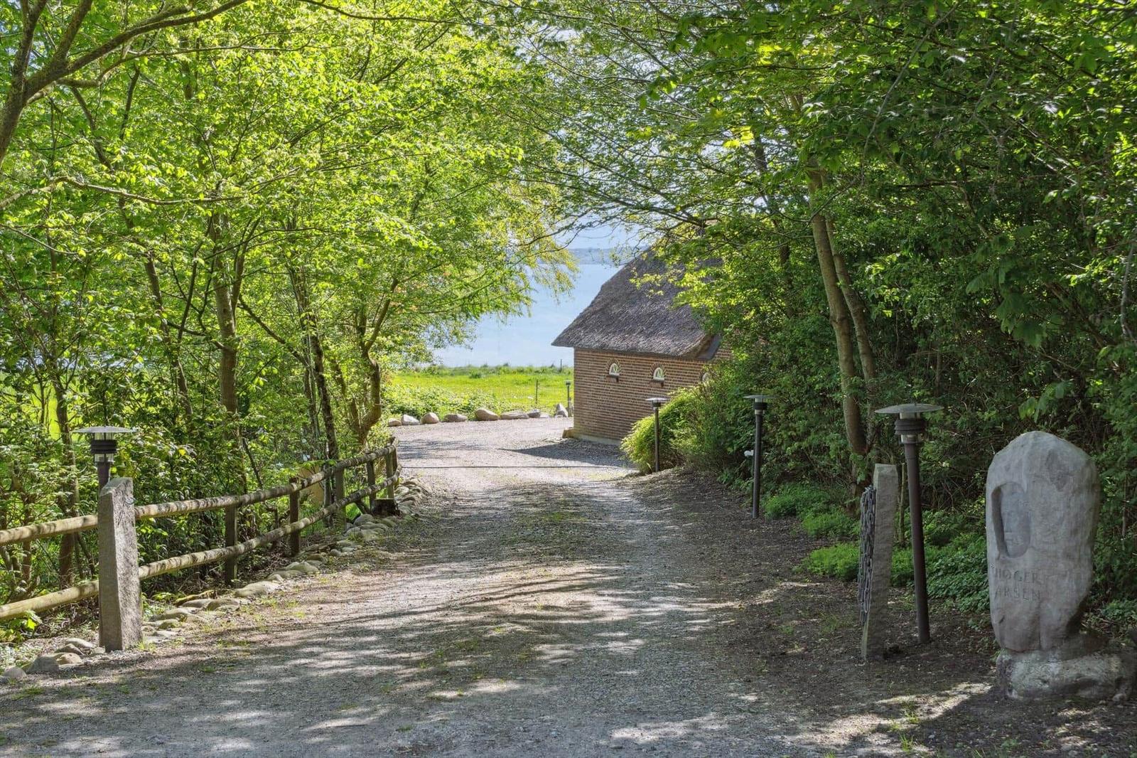 Durch einen Waldweg führt zu einer Hütte mit Strohdach und Blick aufs Wasser.