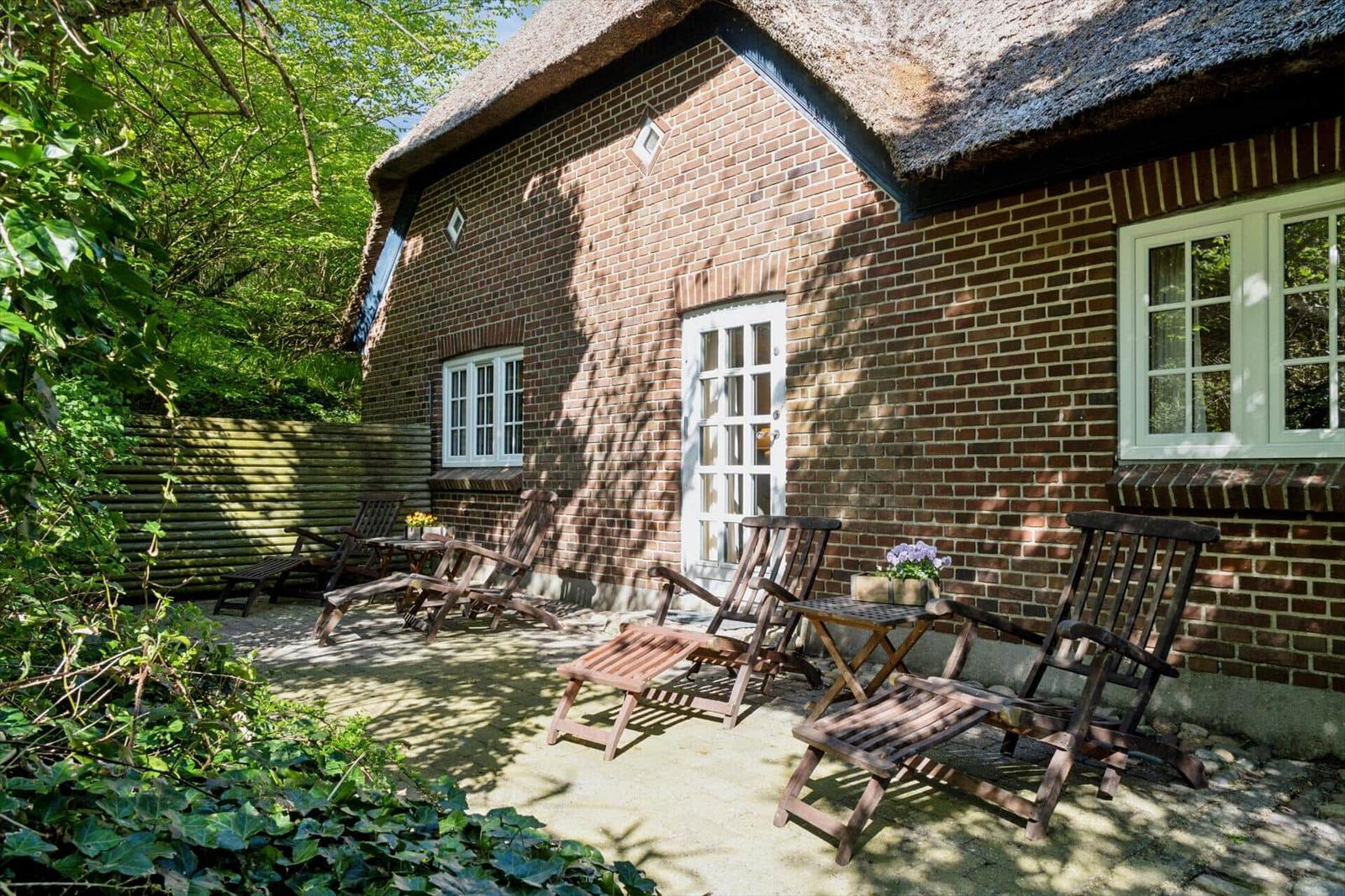 Hinterhof mit Holzstühlen und Tisch vor einem Backsteinhaus mit Strohdach.