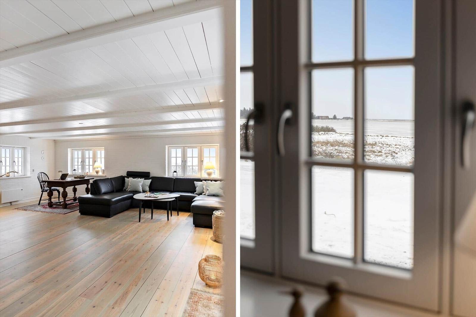 Wohnraum mit schwarzer Couch und Holzboden. Blick durch Fenster auf schneebedecktes Feld.