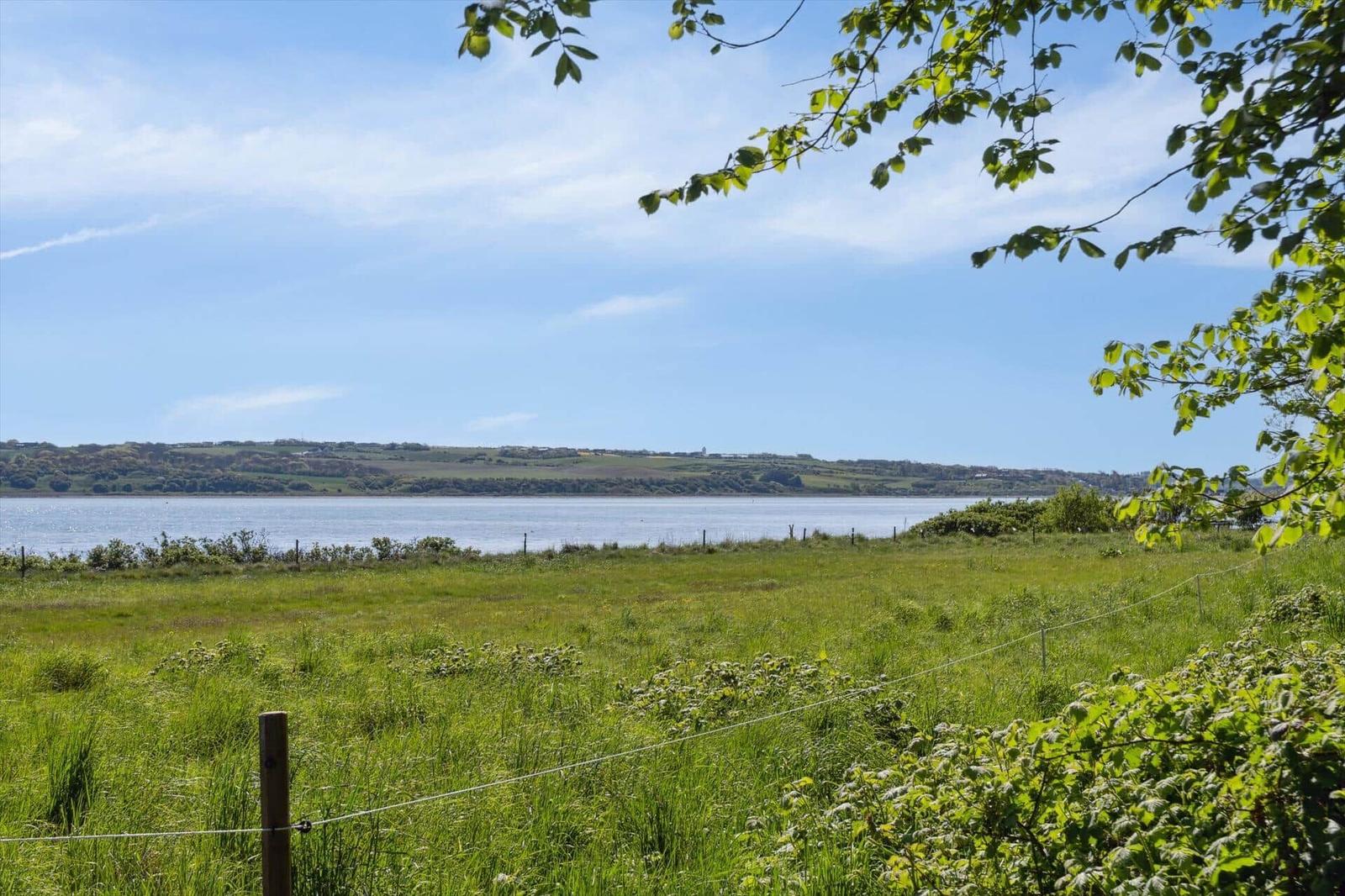 Grünes Feld mit Blick auf einen See und Hügel unter blauem Himmel.