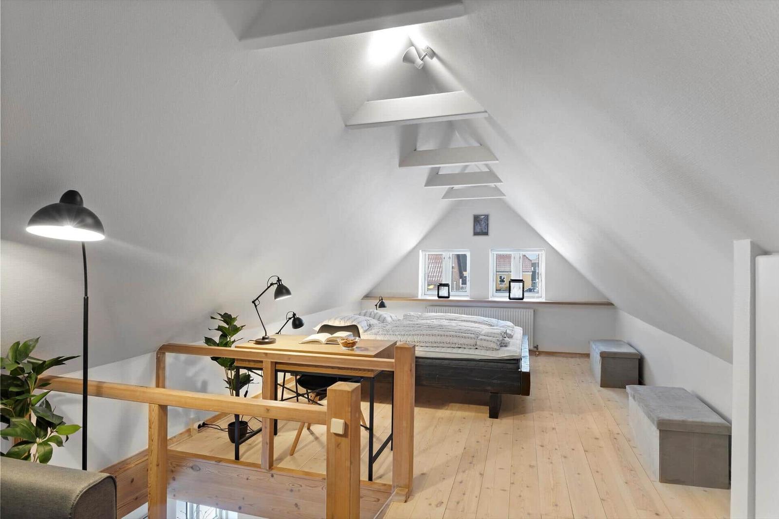 Schlafzimmer mit Dachschrägen, Holzboden und Arbeitsplatz mit Tisch und Stuhl.