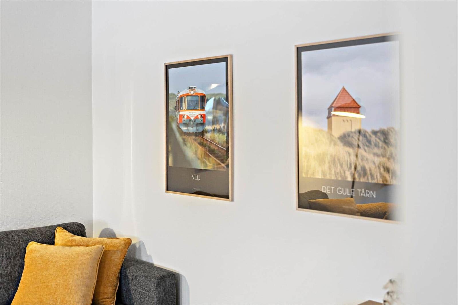 Zwei gerahmte Poster an der Wand über einem Sofa mit Kissen.
