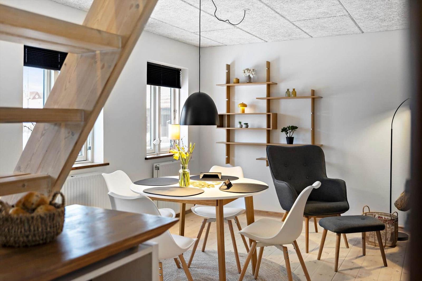 Essbereich mit runden Tisch, weißen Stühlen und Holzregalen an der Wand.