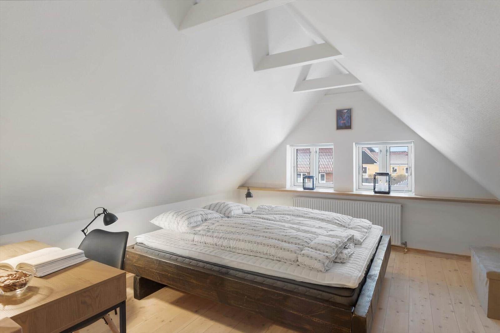 Schlafzimmer mit Dachschrägen, Bett, Schreibtisch und Fenster.