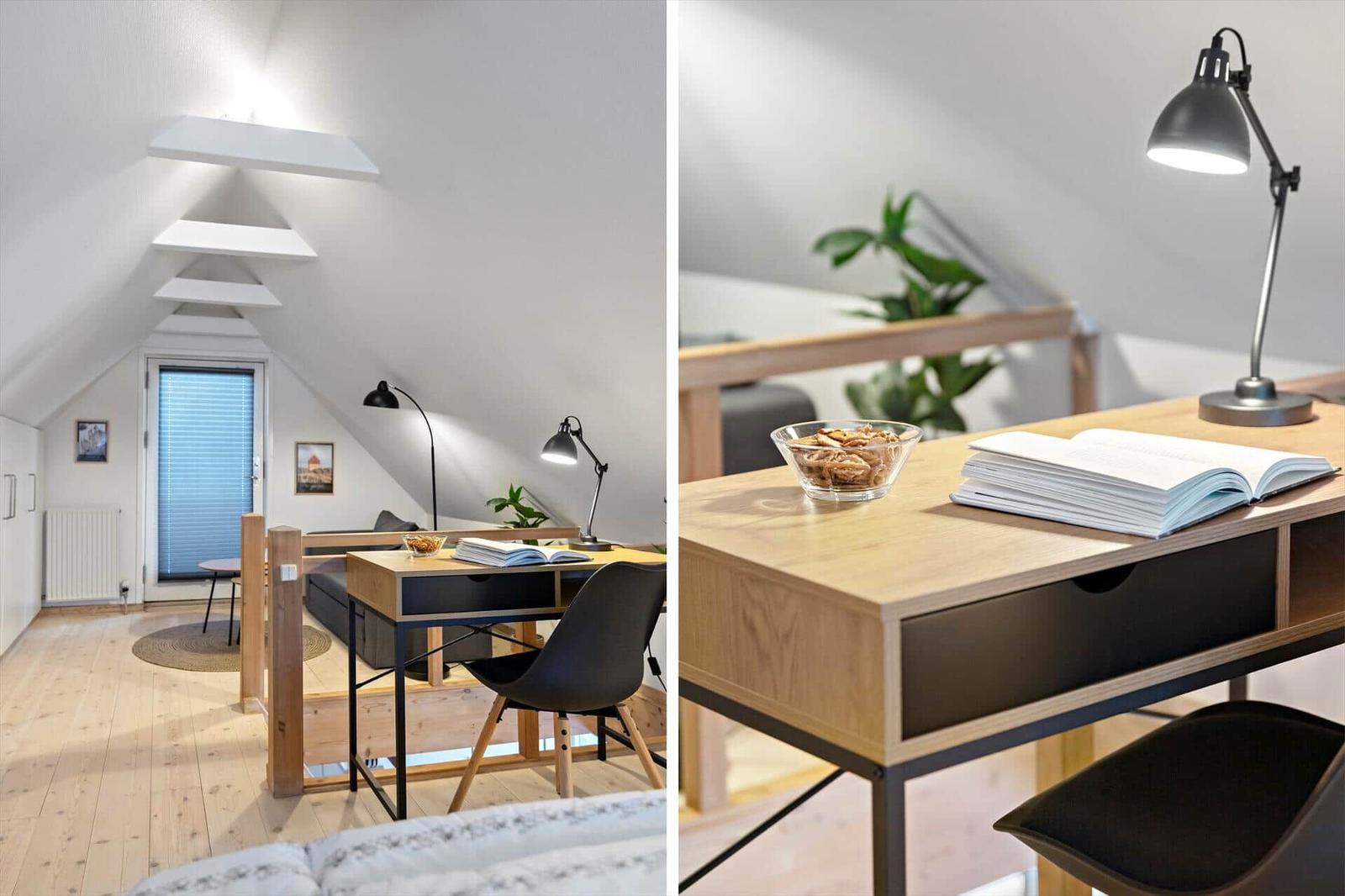Schreibtisch mit Lampe und Buch in einem Dachzimmer mit Holzboden und Fenster.